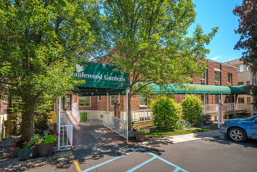 Entrance of Maplewood Gardens with green awning and trees.