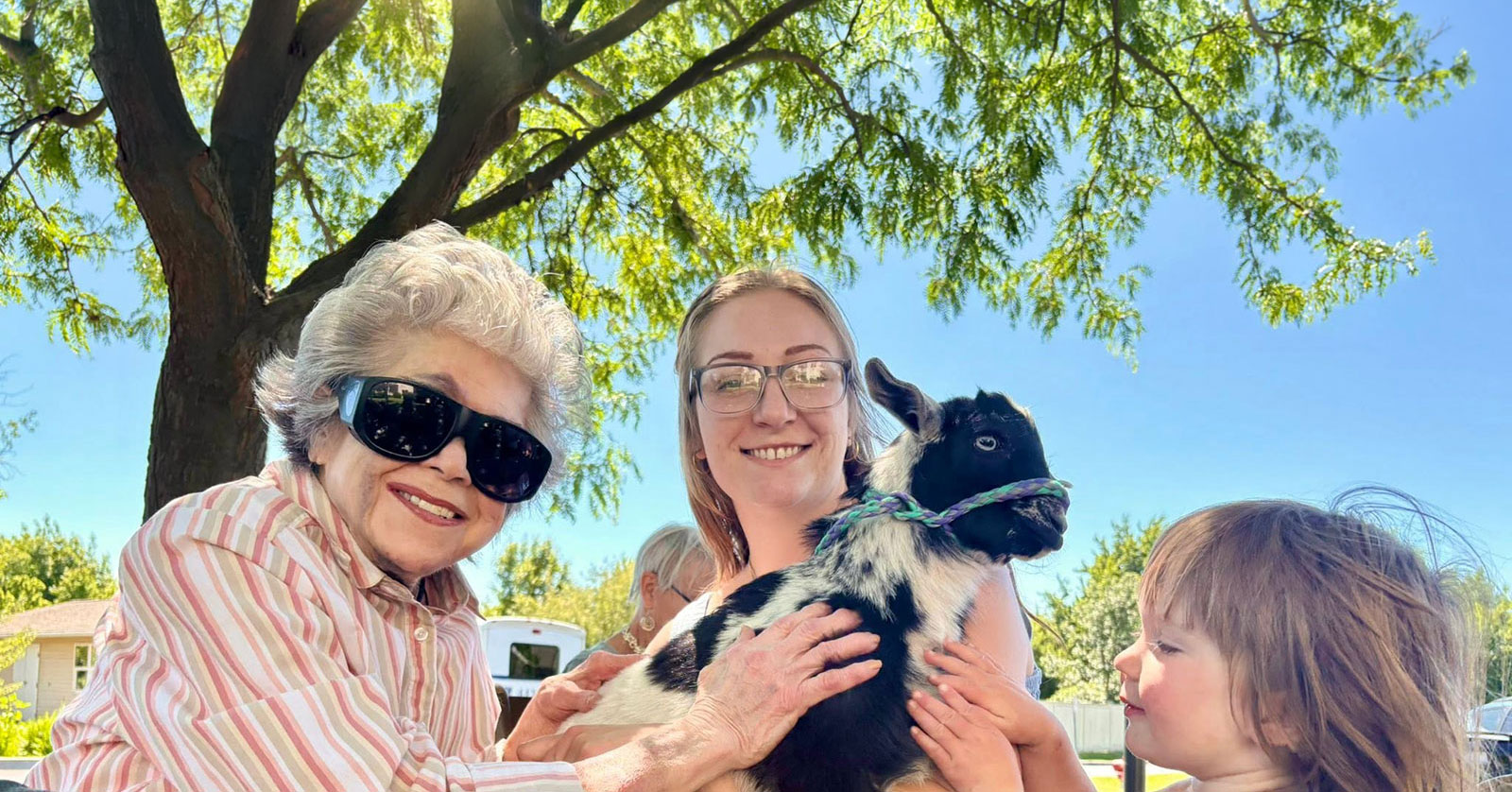 Smiling women and child holding a goat outdoors.