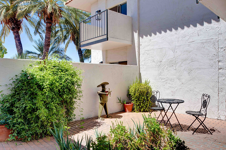 Lush garden patio with seating and palm trees.