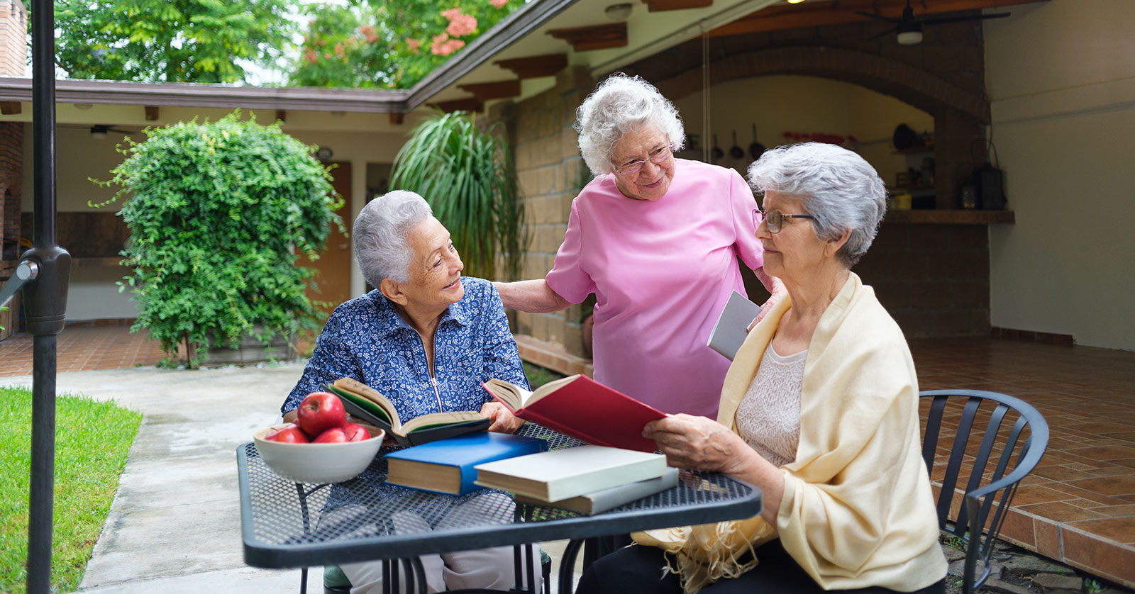 Three elderly women reading and chatting outdoors.
