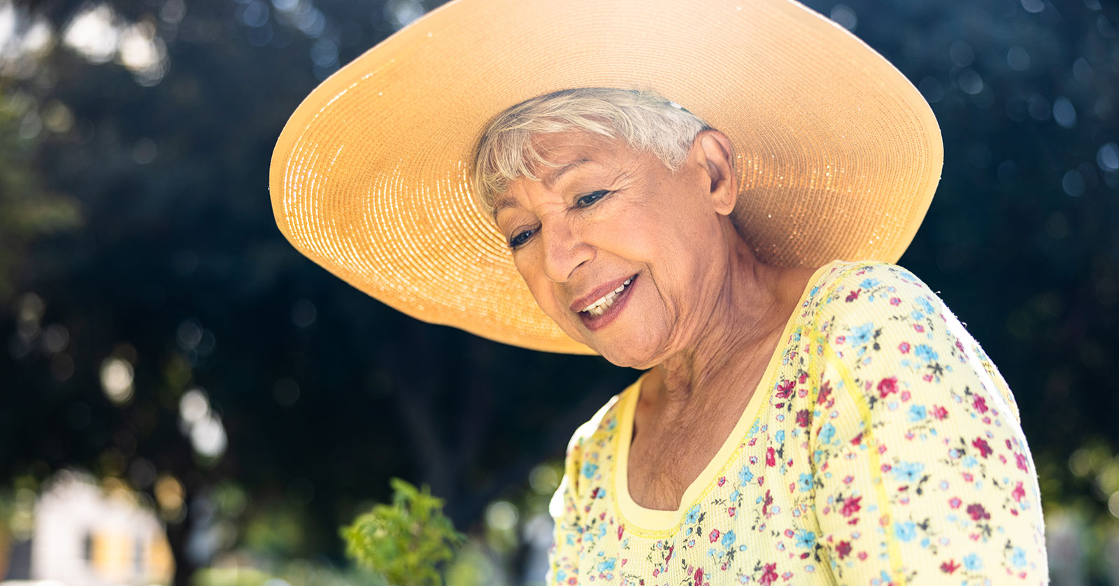 Smiling woman in a sun hat tending to plants.