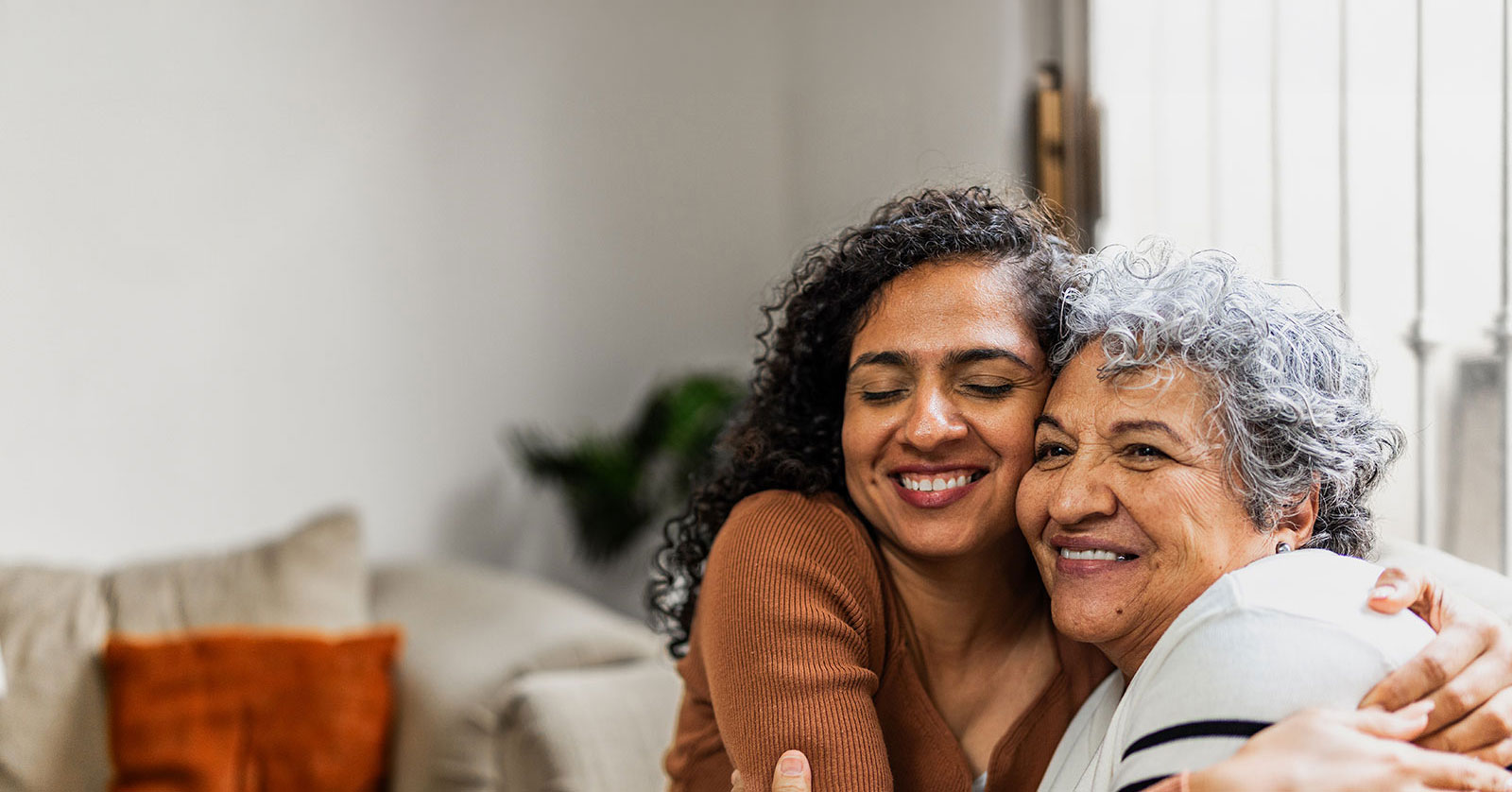 Two women embracing, smiling warmly in a cozy room.