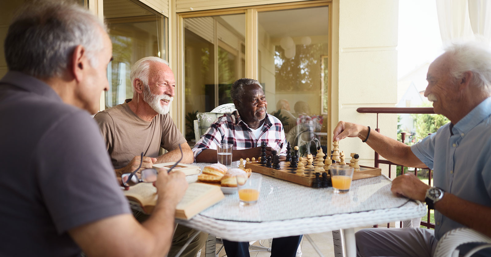 Four friends enjoying chess and conversation on a patio.