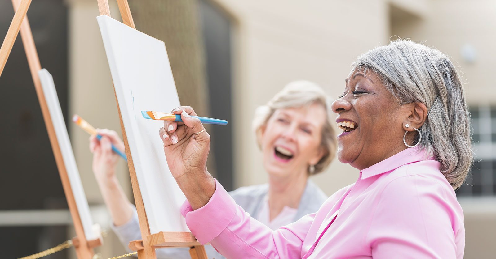 Women joyfully painting on canvases outdoors.