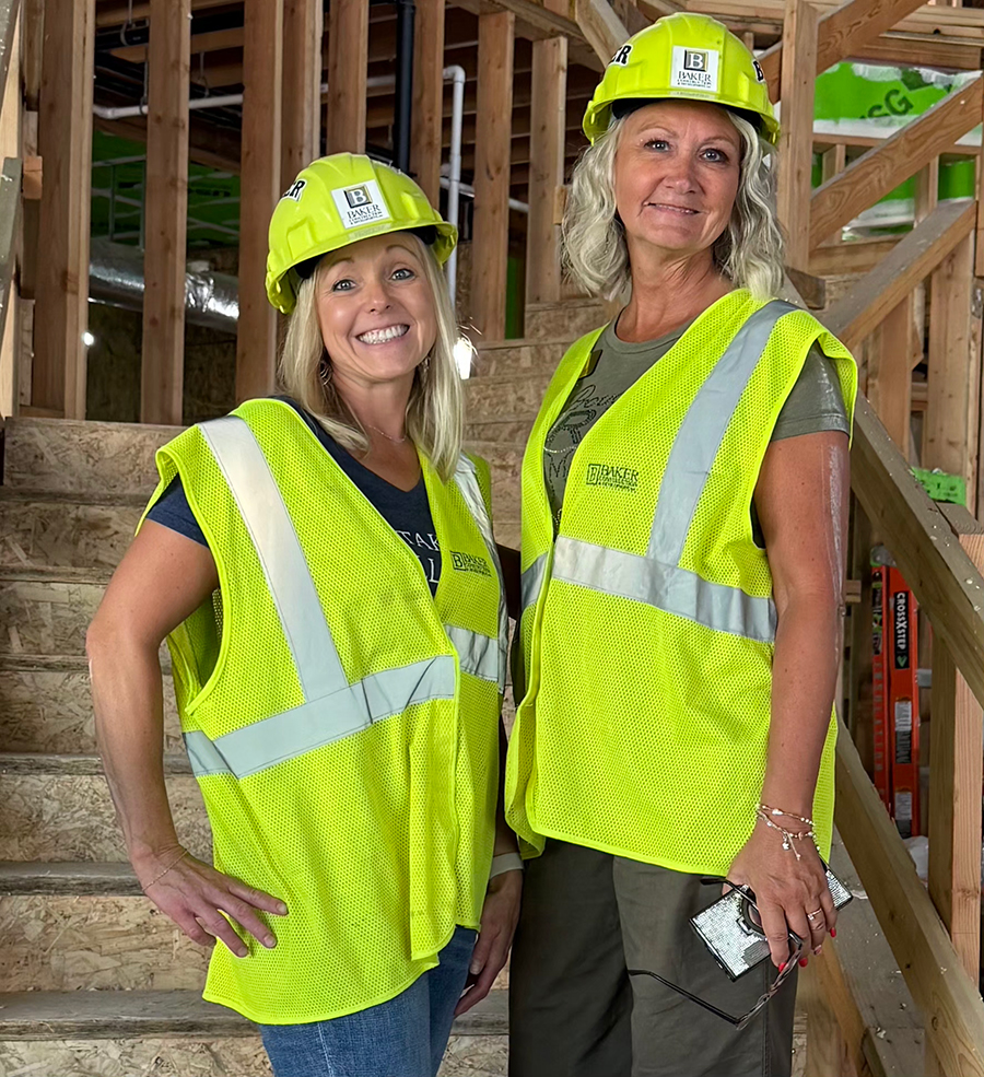 Women in safety gear pose on construction site stairs.
