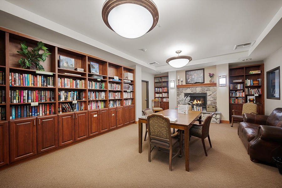 Cozy library with bookshelves, seating, and a fireplace.