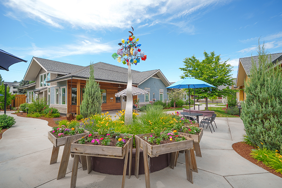 Colorful garden with sculptures and modern homes in background.