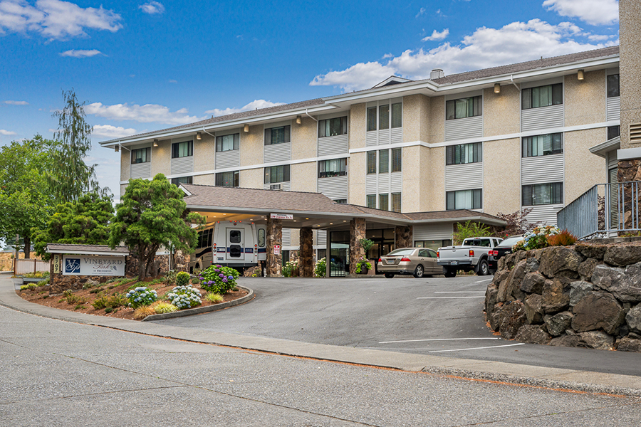 Hotel entrance with parking and landscaped surroundings.