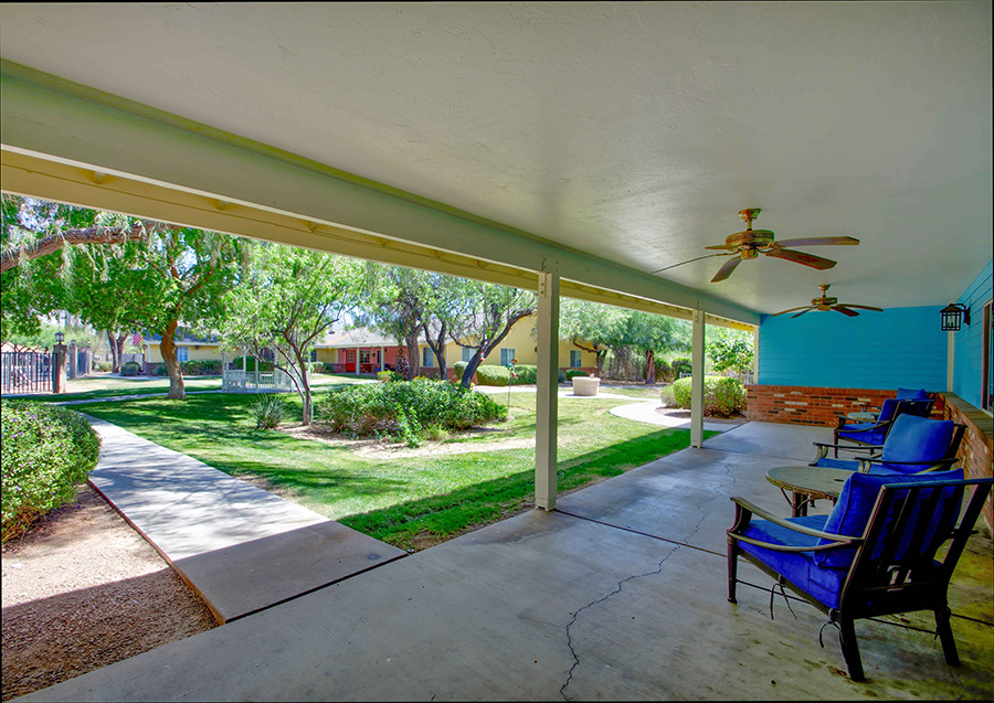 Shaded porch overlooking a green courtyard with trees.