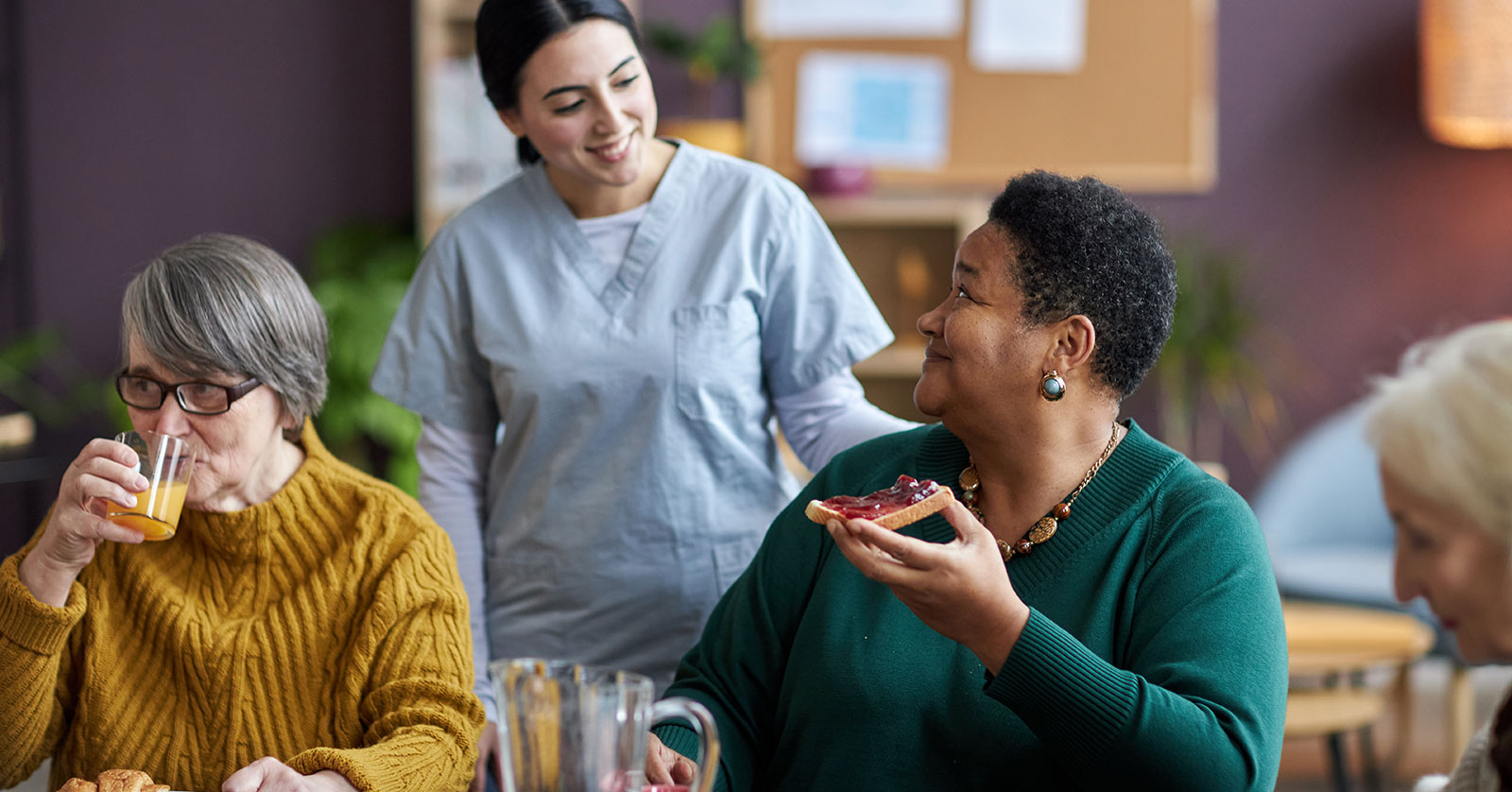 Young nurse assisting senior people during breakfast in retirement home