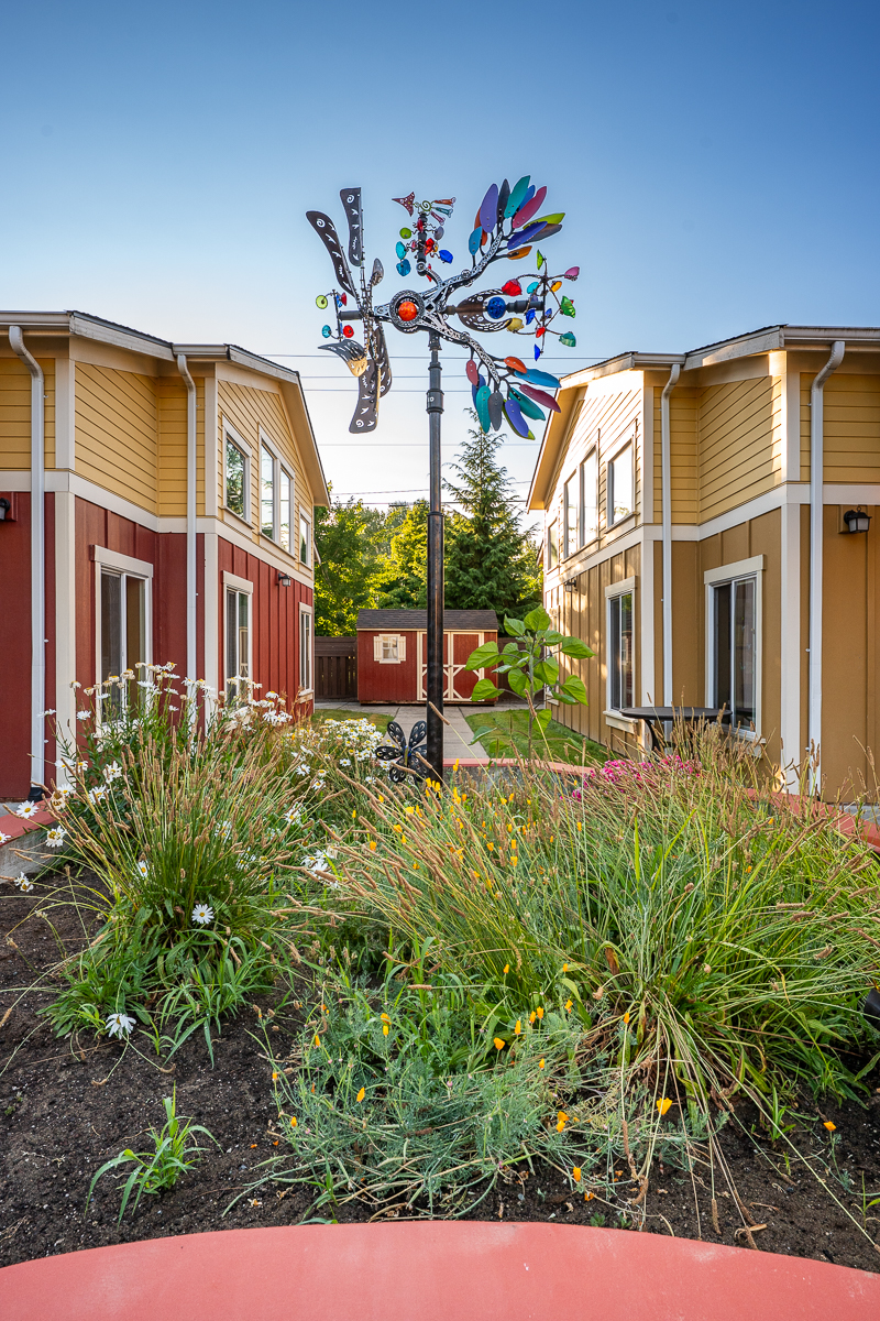 Colorful wind sculpture in a garden between two buildings.