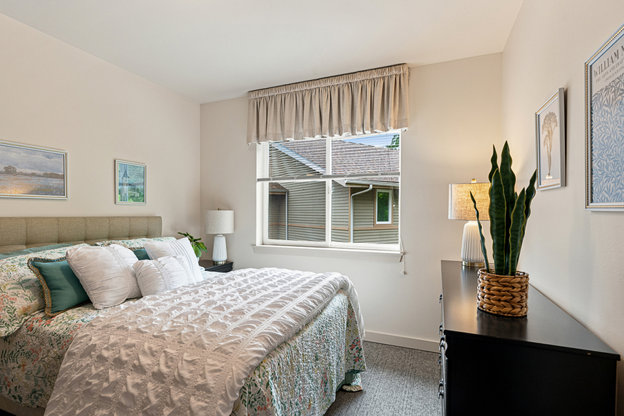 Cozy bedroom with window, plants, and decorative pillows.