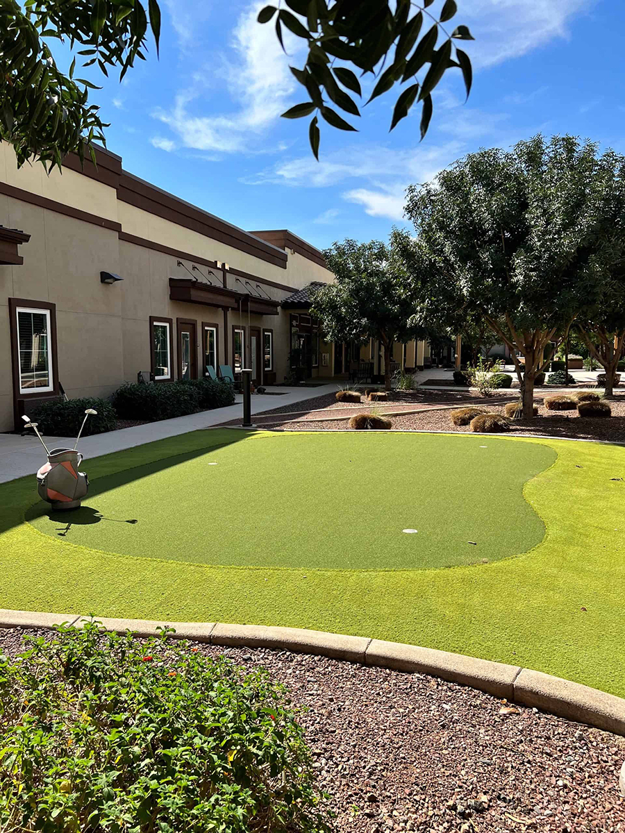 Artificial putting green outside a building with landscaping.