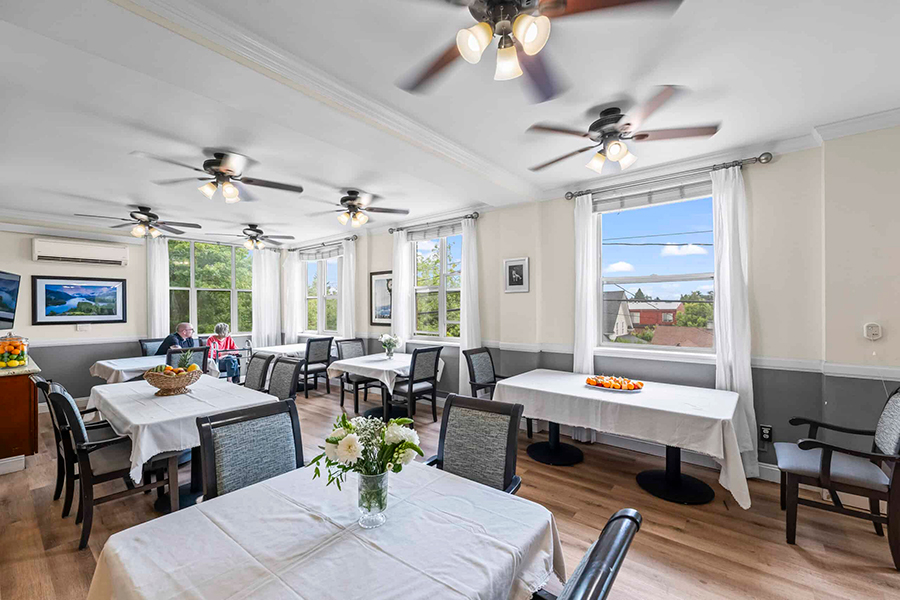 Bright dining room with tables, flowers, and two people.