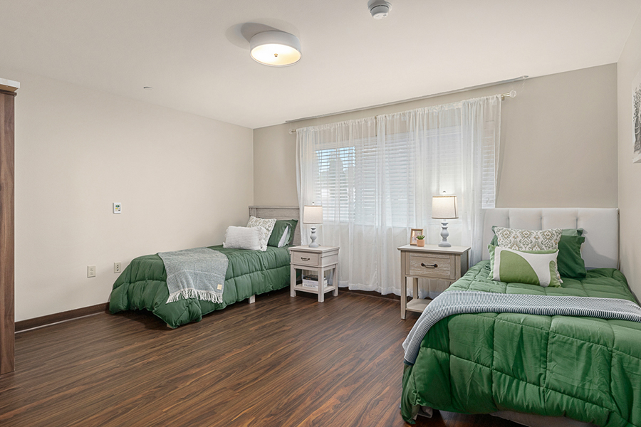 Bright bedroom with green bedding and wooden floors.