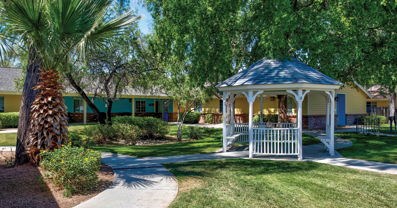 Lush garden with gazebo and colorful houses in background.