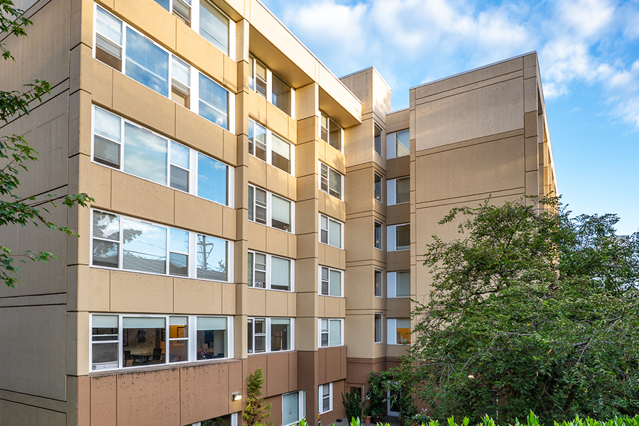 Modern multi-story building with large windows and greenery.