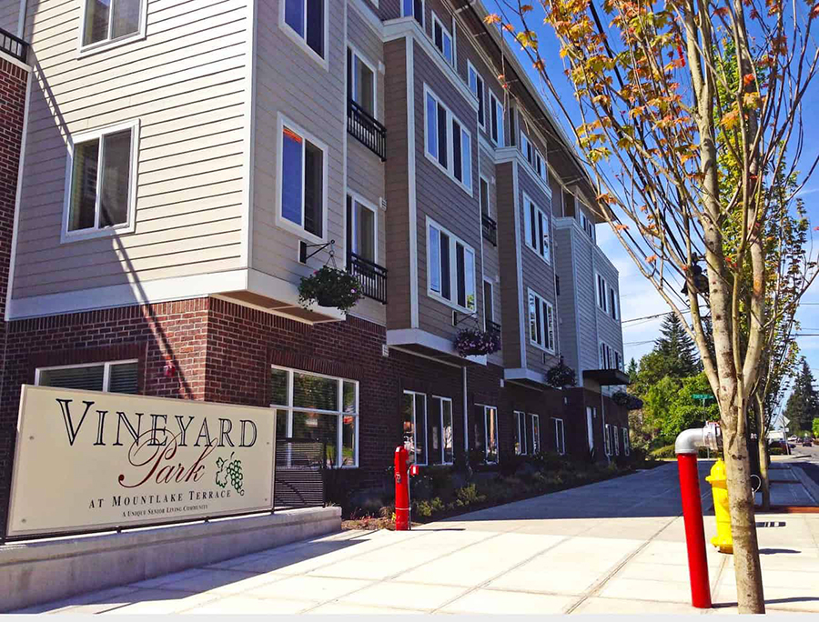 Modern apartment building with landscaped entrance and sign.
